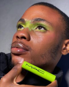 A man with green MAC makeup on his face, creating a striking and vibrant appearance.